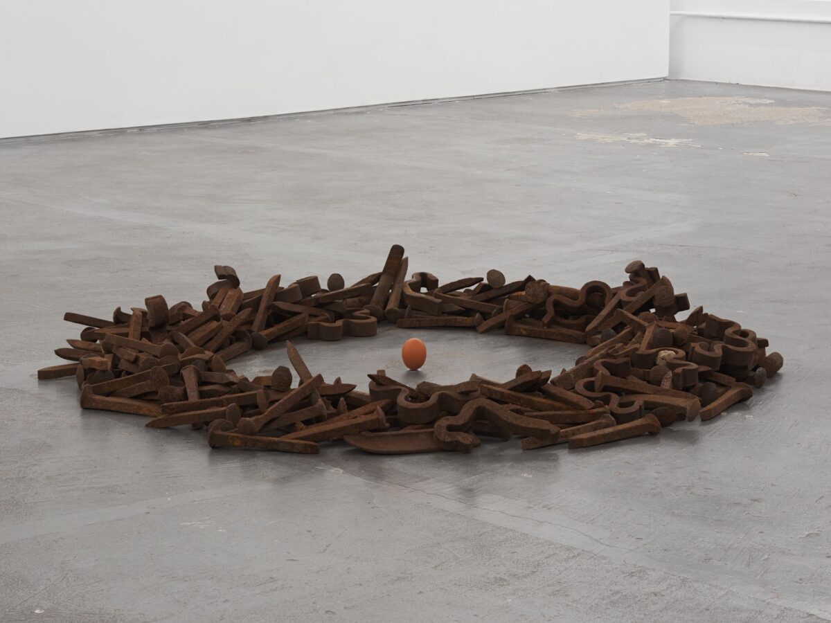This image depicts an artwork by Alannah Farrell titled "Shell Game." This artwork was created in 2026 and its dimensions are not known. Its medium is Iron train spikes hand-gathered on site, antique cobbler’s hammer, raw egg.